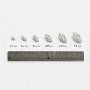 Loose marquise cut diamonds from 0.5mm to 4.5mm placed next to a metal metric ruler for scale.