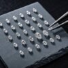 A collection of small, high quality loose pear shaped diamonds meticulously arranged on a dark stone slate with jewelry tweezers.