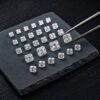 Square radiant cut loose diamonds in different millimeter sizes arranged neatly on a black stone tray with jewelry tweezers.