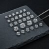 Wholesale cushion cut lab grown diamonds arranged by size on a dark stone tray with tweezers.