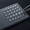 Wholesale princess cut lab grown diamonds arranged by size on a dark stone tray with tweezers.
